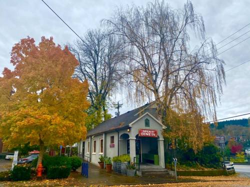 A quaint diner surrounded by colorful autumn trees under a cloudy sky.