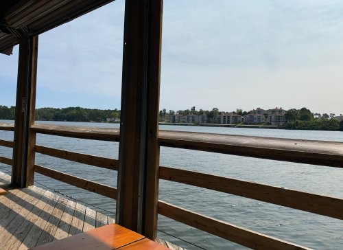 View from a wooden deck overlooking a calm river and distant buildings under a clear sky.