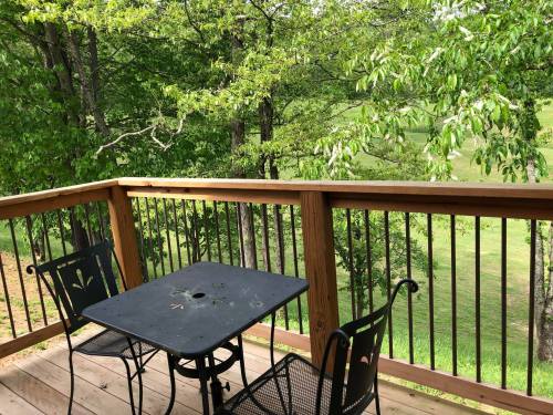A wooden deck with a black table and two chairs, surrounded by lush green trees and grass.