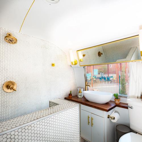Modern bathroom with hexagonal tile, a freestanding sink, gold fixtures, and a large window overlooking an outdoor area.