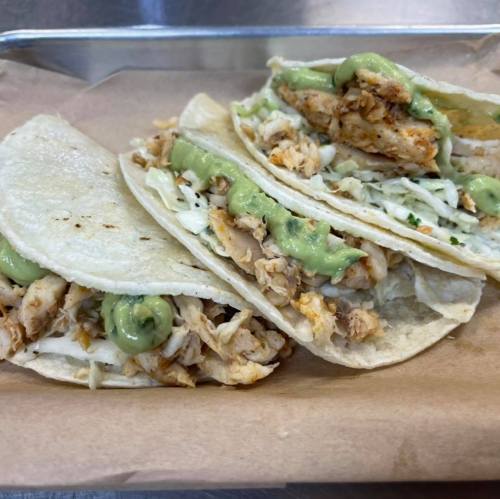 Three tacos on a tray, filled with shredded chicken, cabbage, and topped with green sauce.