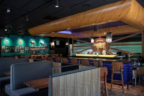 Interior of a modern restaurant featuring wooden accents, a bar area, and cow-themed decor on the walls.