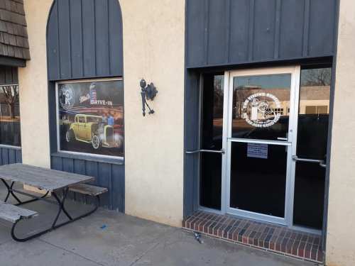 Exterior view of a drive-in restaurant featuring a vintage car mural and a glass door entrance. Picnic table nearby.