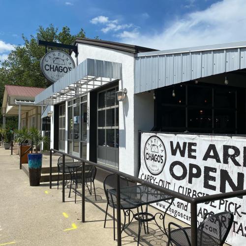 Exterior of Chago's restaurant with outdoor seating and a sign stating "We Are Open" for carry-out and curbside pick-up.