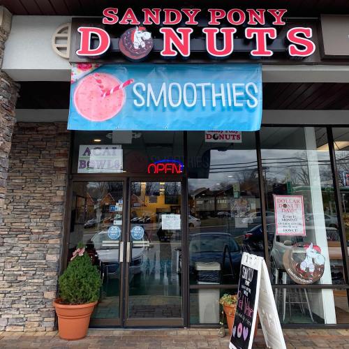 Exterior of Sandy Pony Donuts shop with a sign for smoothies and acai bowls, featuring a welcoming entrance.
