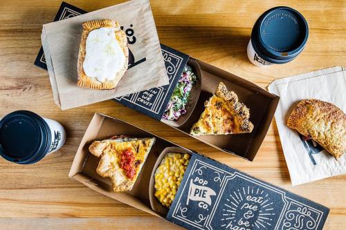 A wooden table with various pie boxes, a salad, mac and cheese, and coffee cups.