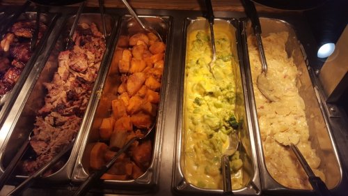 A buffet with various dishes: pulled pork, sweet potatoes, broccoli in cheese sauce, and creamy potatoes.