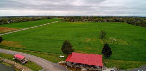 Aerial view of a green landscape with a red-roofed building, a road, and a small cemetery in the distance.