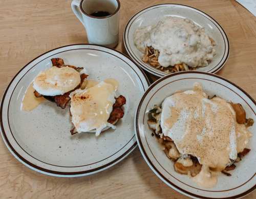 A breakfast spread featuring two plates: one with eggs Benedict and the other with biscuits and gravy, plus a cup of coffee.