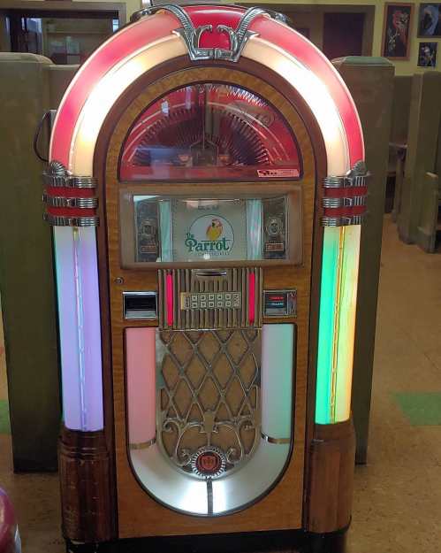 A vintage jukebox with colorful lights and a wooden finish, featuring a Parrot logo on the front.