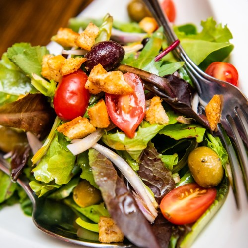 A fresh salad with mixed greens, cherry tomatoes, olives, croutons, and a light dressing, served in a bowl.