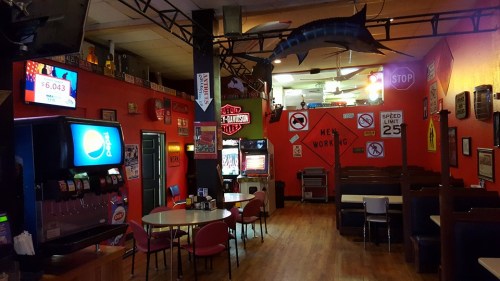 A colorful diner interior with red walls, vintage signs, tables, and a soda machine, creating a lively atmosphere.