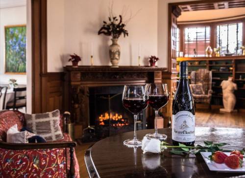 A cozy room with a fireplace, featuring two glasses of red wine, a bottle, and a rose on a table.