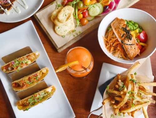 A vibrant spread of tacos, salmon salad, fries, and a colorful drink on a wooden table.