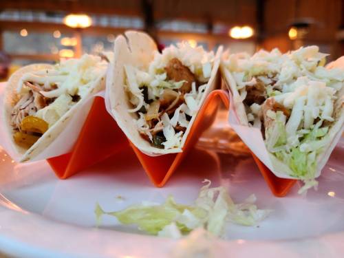 Three tacos filled with meat, vegetables, and shredded cheese, served on a plate with some lettuce scattered around.