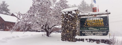 Snow-covered sign for Northern Outdoors Resort, surrounded by trees and a winter landscape.