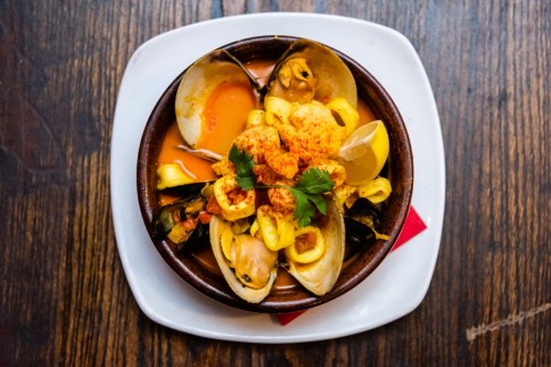 A bowl of seafood pasta with clams, mussels, and a rich orange sauce, garnished with cilantro and lemon wedges.