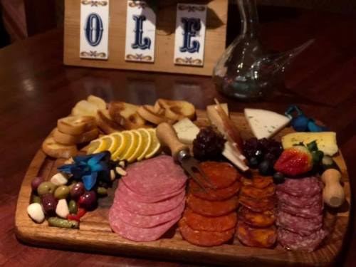 A wooden platter filled with assorted meats, cheeses, fruits, nuts, and crackers, with decorative blue flowers.