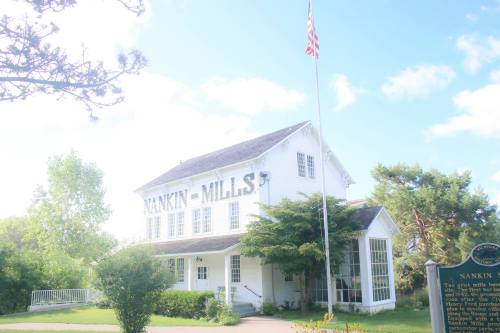 Historic Nankin Mills building with an American flag, surrounded by greenery and a blue sky.