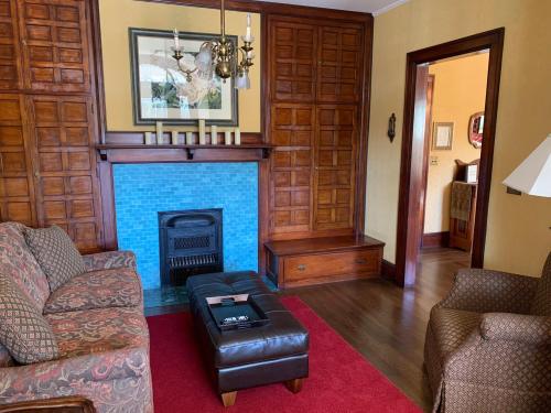 Cozy living room with wooden paneling, a blue-tiled fireplace, patterned sofas, and a coffee table on a red rug.