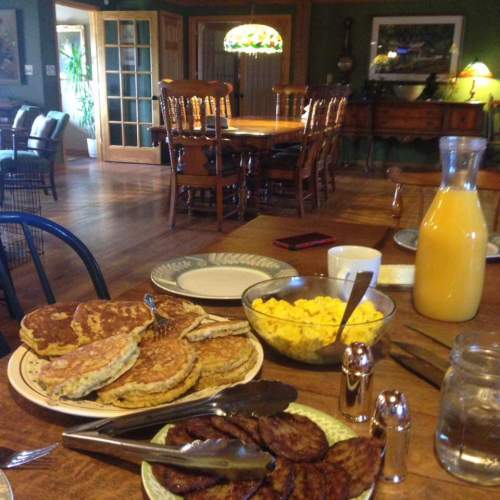A cozy dining table set with pancakes, scrambled eggs, sausage, orange juice, and a warm, inviting interior.