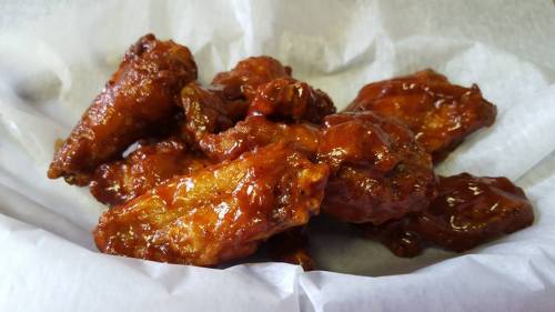 A close-up of glazed chicken wings piled on a white paper-lined basket.
