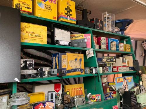 A colorful display of vintage cameras and camera accessories on a green shelf, showcasing various retro packaging and designs.