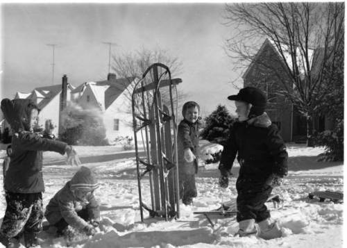 Children playing in the snow, with a sled and houses in the background, enjoying a winter day.