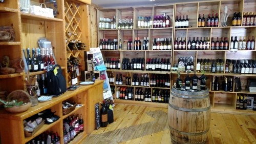 A cozy wine shop featuring wooden shelves filled with various bottles of wine and a barrel in the center.