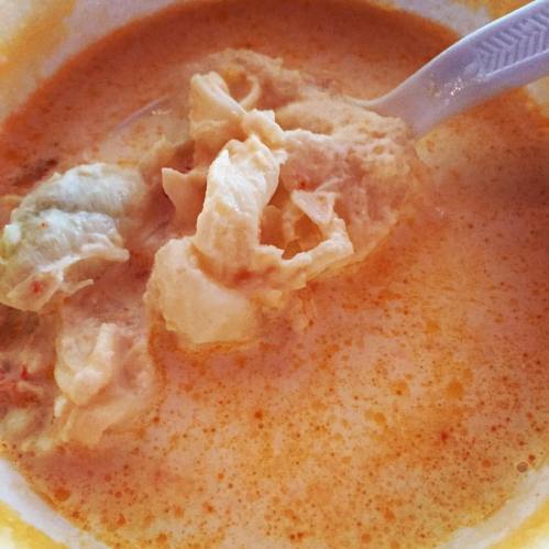 A close-up of a creamy soup with chunks of meat and a spoon, showcasing a rich, orange broth.