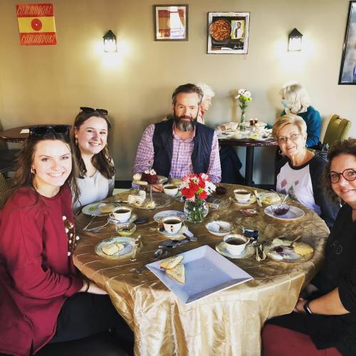 A group of five people enjoying dessert and coffee at a cozy café table, decorated with flowers.