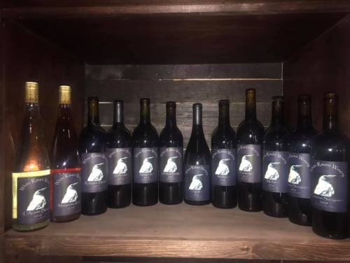 A wooden shelf displaying various bottles of wine, each with a label featuring a raven logo.