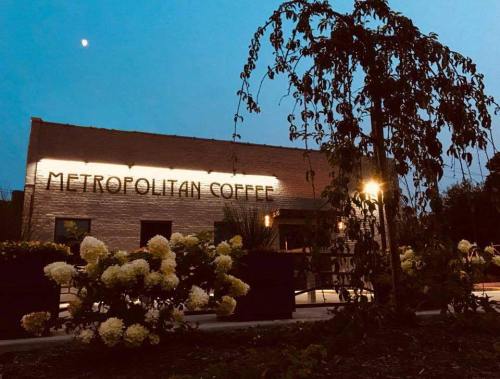A cozy coffee shop named "Metropolitan Coffee" illuminated at dusk, surrounded by flowers and a tree.