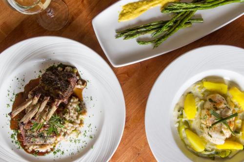 A beautifully plated meal featuring lamb chops, risotto, asparagus, and a creamy seafood dish with yellow squash.