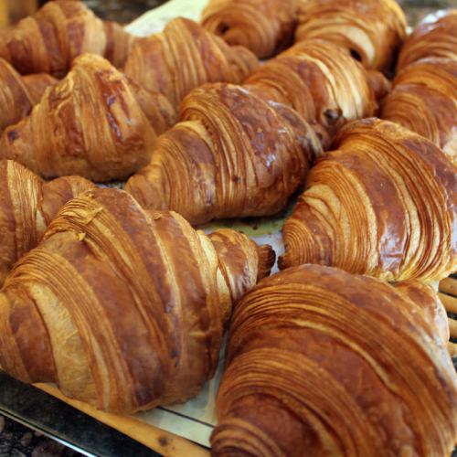 Freshly baked golden-brown croissants arranged on a baking tray, showcasing their flaky layers.