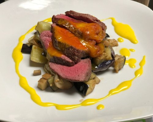 Sliced steak atop roasted eggplant, drizzled with a vibrant yellow sauce on a white plate.