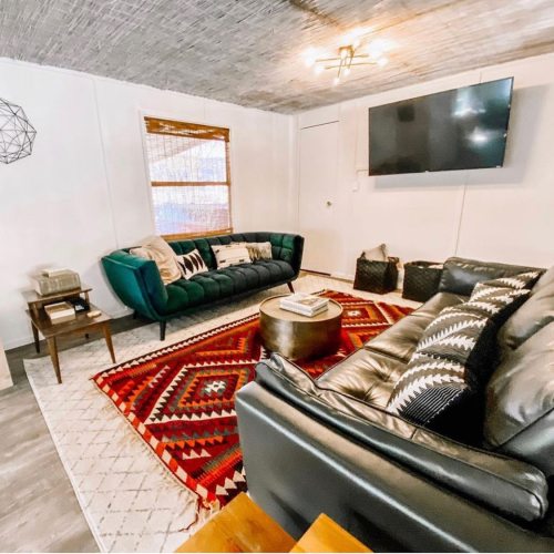 Cozy living room with green and black sofas, a round coffee table, and a patterned rug under a modern light fixture.