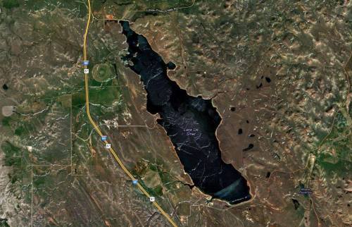 Aerial view of a large, dark lake surrounded by rugged terrain and highways in a rural area.