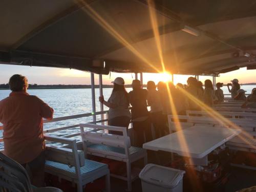 People enjoying a sunset view from a boat, with sunlight streaming across the water.