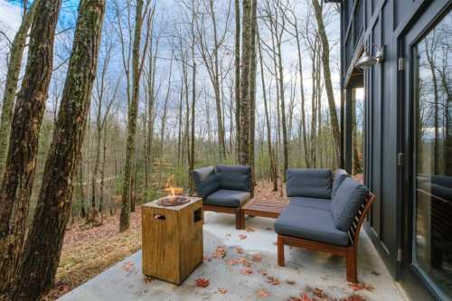 Cozy outdoor seating area with fire pit, surrounded by tall trees and a scenic view.