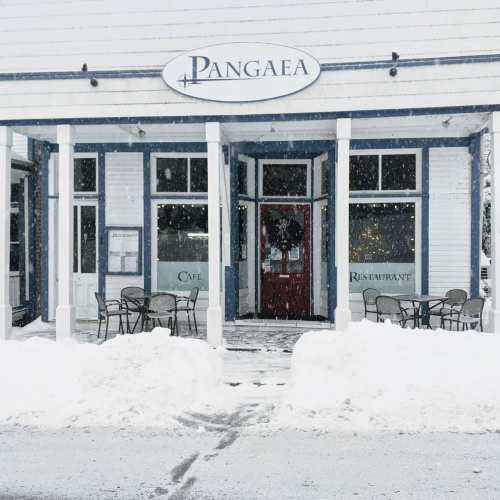 Snowy scene of Pangaea restaurant with outdoor seating, surrounded by snowdrifts and a festive wreath on the door.