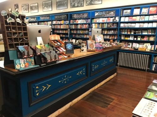 A cozy bookstore interior featuring a colorful display of books and a wooden checkout counter with a computer.