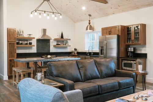 Modern kitchen and living area featuring a sofa, stainless steel appliances, and wooden accents with a high ceiling.