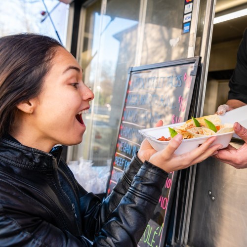 A woman excitedly receives a food order from a vendor at a food truck.