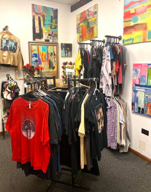 A clothing rack filled with various t-shirts in a colorful boutique, surrounded by vibrant artwork on the walls.