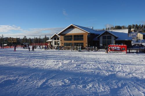 A snowy landscape with a ski lodge and people enjoying winter activities under a clear blue sky.