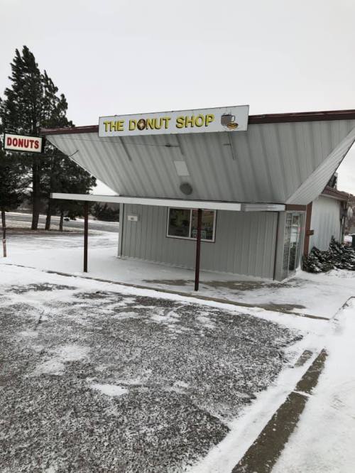 A small, snowy donut shop with a sign reading "The Donut Shop" and a display of donuts in the window.