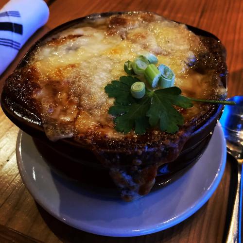 A bowl of cheesy, bubbling French onion soup topped with green onions and parsley, served on a white plate.