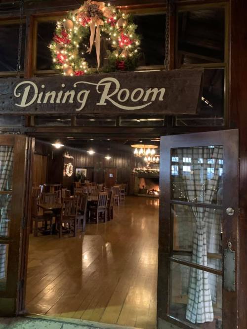 Cozy dining room entrance decorated for the holidays, featuring wooden tables and a warm fireplace.