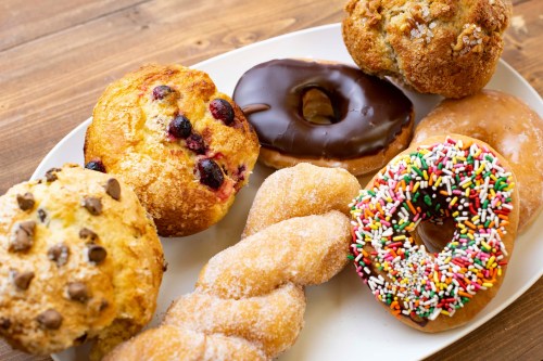 A variety of baked goods on a plate, including muffins, donuts, and a colorful sprinkle donut.